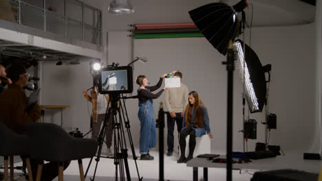 Female-Assistant-Uses-Clapperboard-As-Actors-Shoot-Movie-Or-Video-In-Studio-With-Film-Crew-And-Director-Shot-In-Real-Time